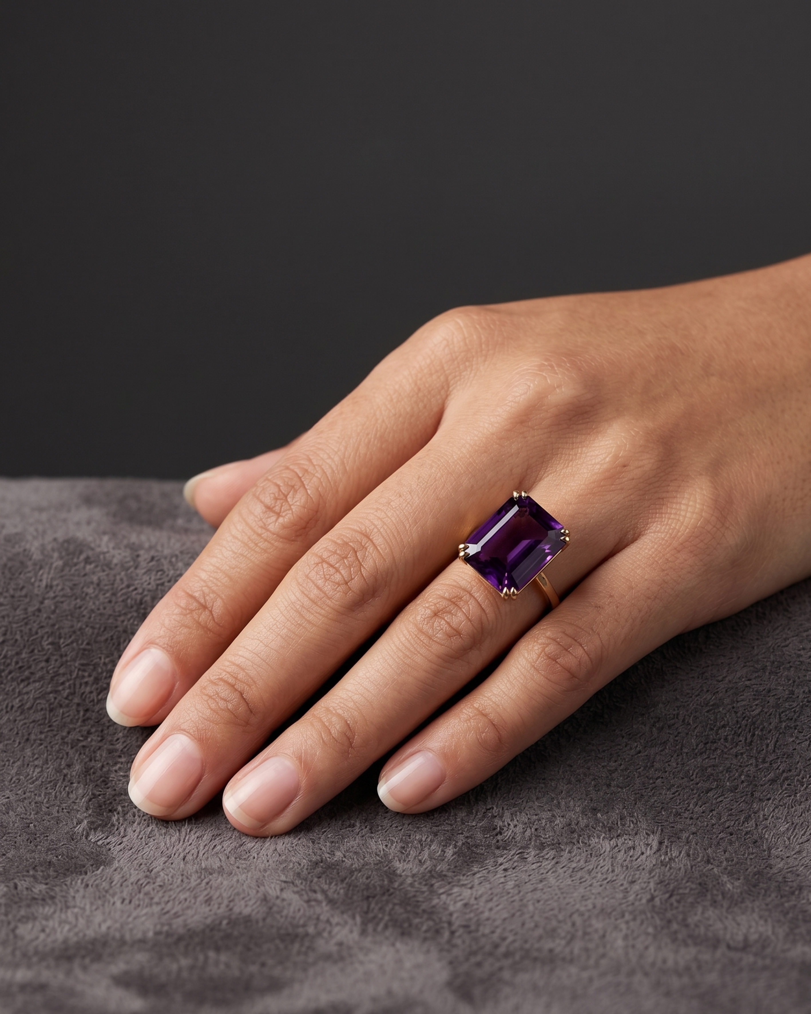 A model's hand wearing the London Bridge ring with a rectangular fancy purple sapphire set in a gold band.