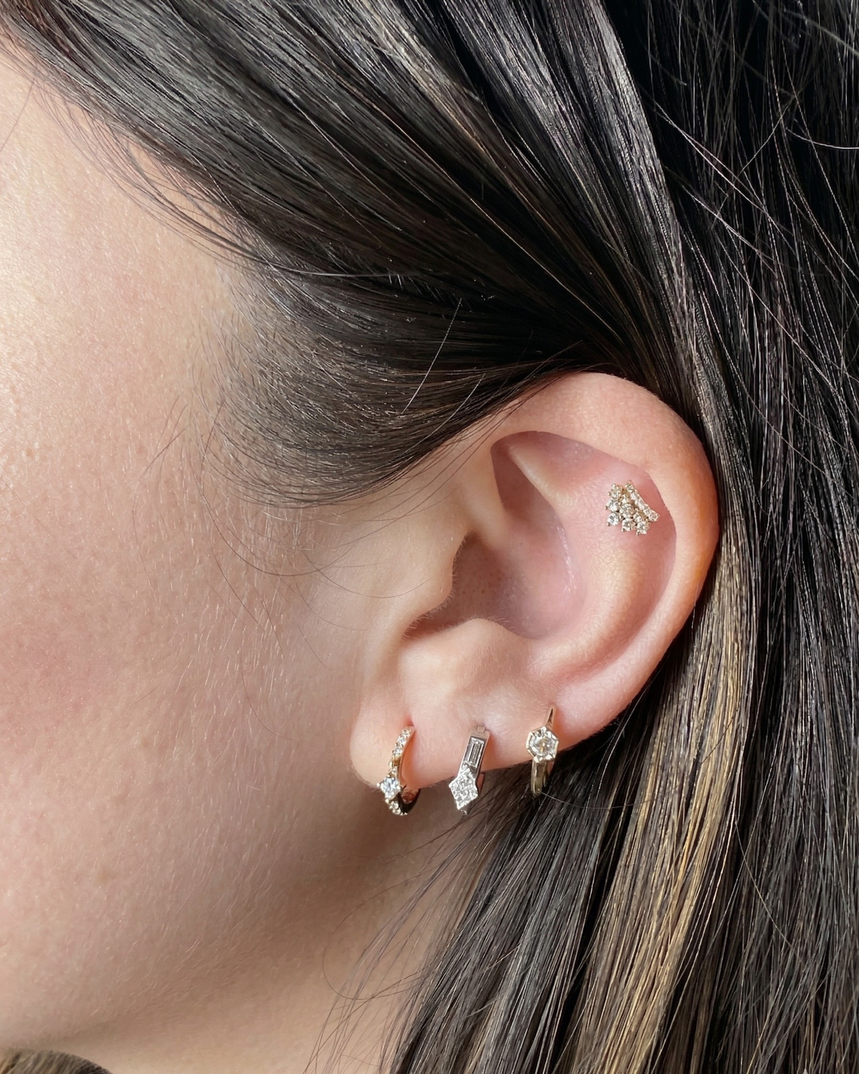 A model's ear with a curated stack featuring the Modernist Triangle and Baguette Diamond Hoop, styled with other diamond earrings.